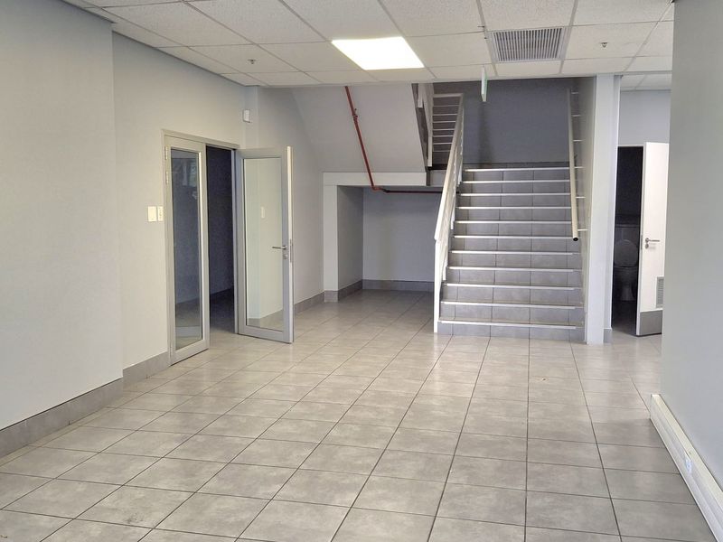 Spacious industrial hallway featuring tiled flooring, a suspended ceiling with recessed lighting, and a central staircase leading to the upper level.
