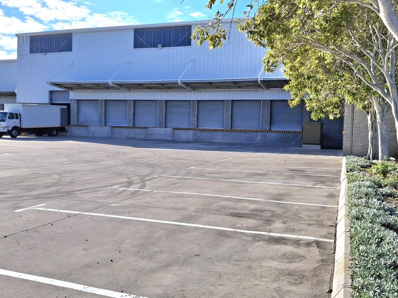 Industrial warehouse exterior featuring multiple roller shutter loading bays, a protective canopy, and a large concrete yard area with marked parking bays.