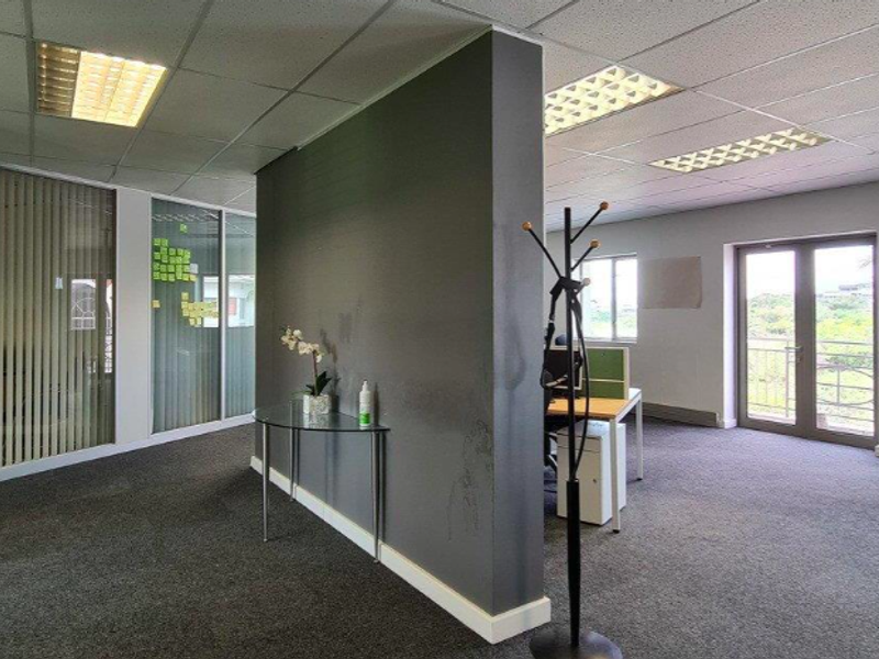 Open plan office space featuring a central partition wall, suspended ceilings with recessed lighting, carpeted floors, and access to an outdoor balcony area.