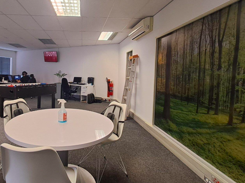 Open-plan office space featuring carpeted flooring, suspended ceiling with recessed lighting, and a wall-mounted air conditioning unit.