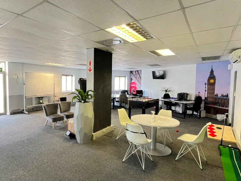 Open-plan office space featuring a suspended ceiling, recessed lighting, carpeted flooring, and a wall-mounted air conditioning unit.