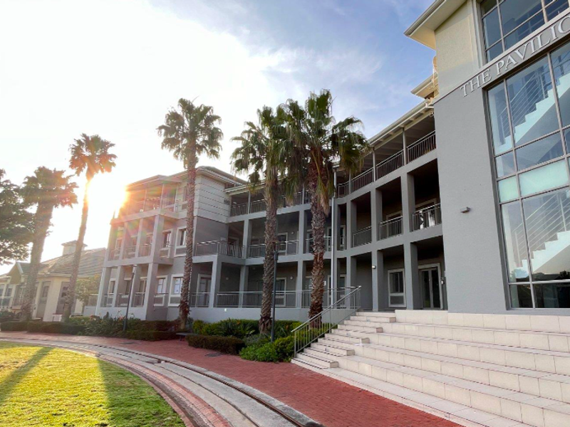 Exterior view of The Pavilion office building featuring multi-level balconies, large glass windows, and a landscaped garden area with paved walkways.