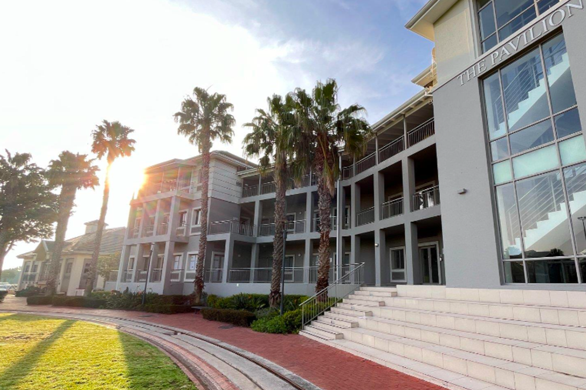 Exterior view of The Pavilion office building featuring multi-level balconies, large glass windows, and a landscaped garden area with paved walkways.