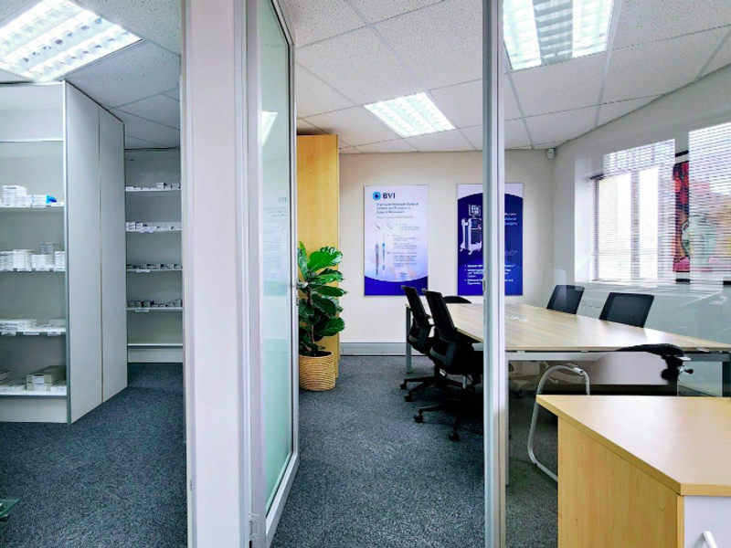 A professional office space featuring glass partitions, carpeted flooring, recessed lighting, and integrated shelving units, suitable for a corporate or medical environment.