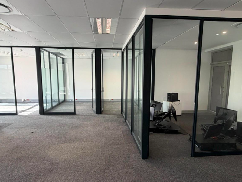 Modern office space featuring glass-partitioned private offices, suspended ceilings, and carpeted flooring, providing a professional and open work environment.