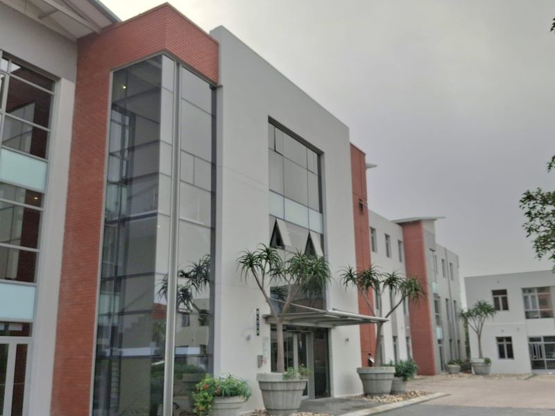 Modern office building exterior featuring a combination of brick and glass curtain wall architecture with a paved entrance area.