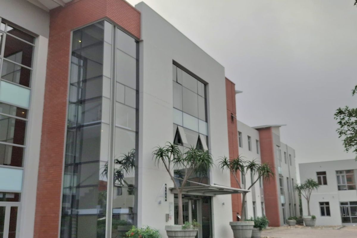 Modern office building exterior featuring a combination of brick and glass curtain wall architecture with a paved entrance area.