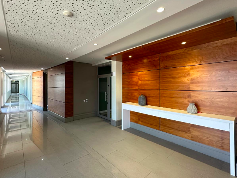 Modern office hallway featuring high-quality wood veneer wall paneling, polished tile flooring, and integrated recessed lighting with acoustic ceiling tiles.