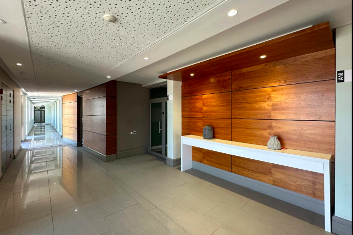 Modern office hallway featuring high-quality wood veneer wall paneling, polished tile flooring, and integrated recessed lighting with acoustic ceiling tiles.