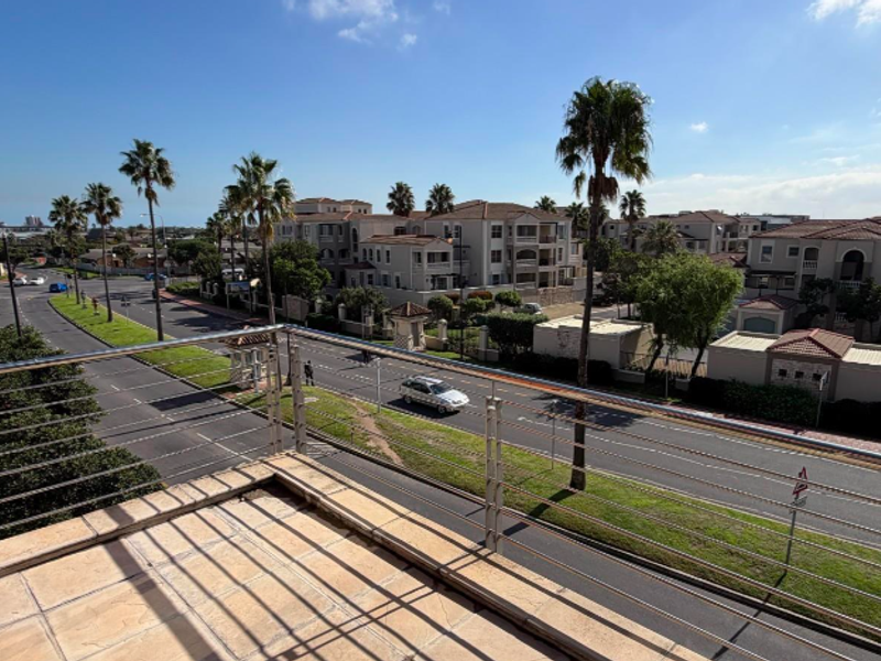 A spacious balcony featuring tiled flooring and a modern stainless steel balustrade, offering an elevated view of the surrounding neighbourhood and street.