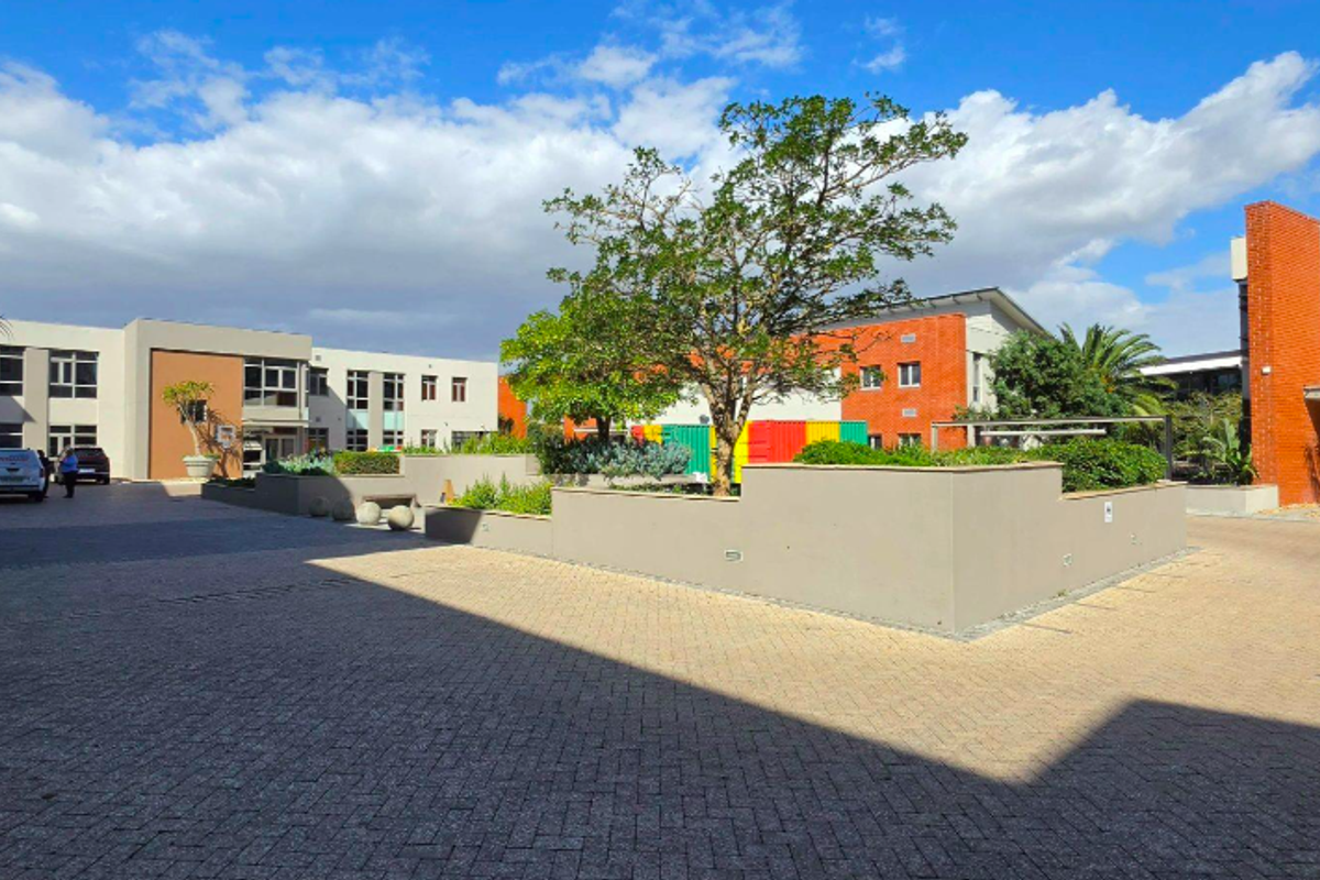 A well-maintained office park courtyard featuring paved surfaces, raised planter beds, and modern building facades.