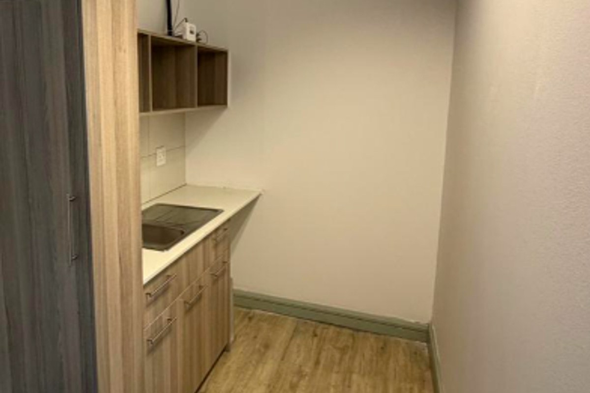 A compact office kitchenette featuring wood-look laminate cabinetry, a stainless steel sink, and durable flooring, providing a functional space for staff.