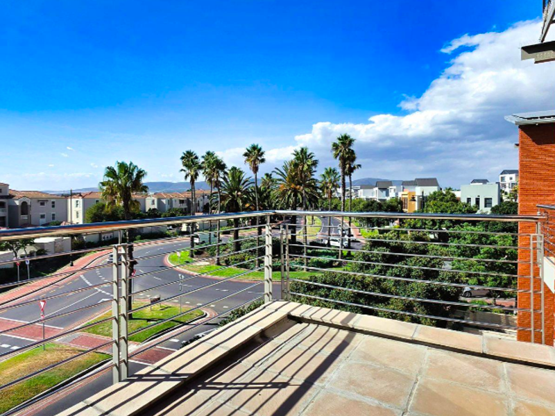 A spacious balcony featuring tiled flooring and a modern stainless steel balustrade, offering an elevated view of the surrounding neighbourhood and streetscape.