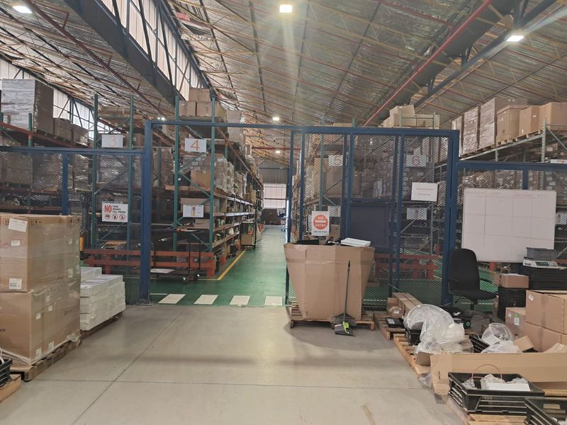 Industrial warehouse space featuring high-bay ceilings, extensive steel racking systems, and secure metal mesh partitioning for organized storage and logistics operations.