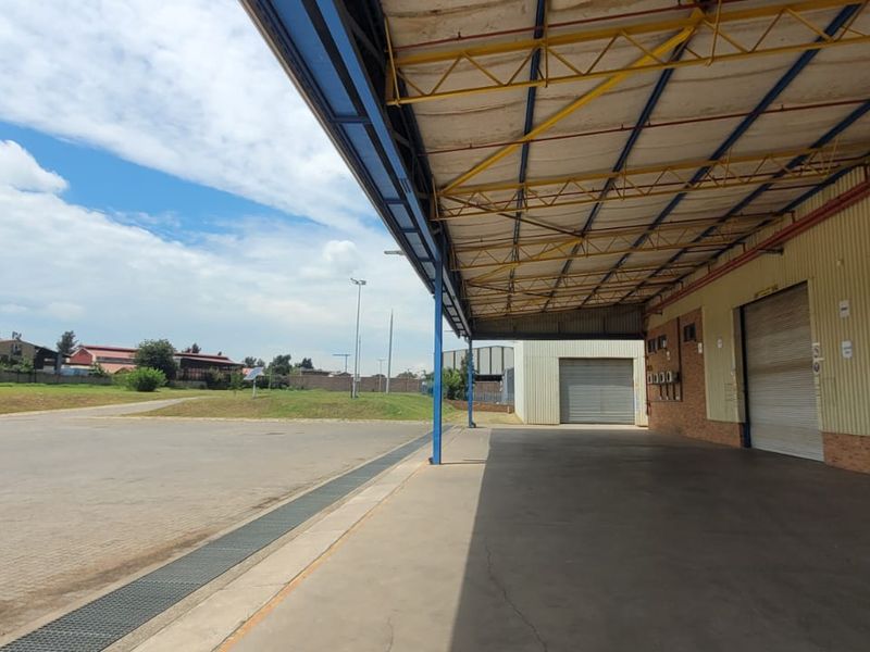 Industrial loading bay area featuring a covered canopy, multiple roller shutter doors, and a spacious concrete hardstand for vehicle access.