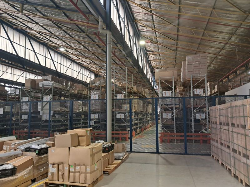 Spacious industrial warehouse featuring high-bay ceilings, concrete flooring, and extensive metal racking systems secured by industrial mesh partitioning.