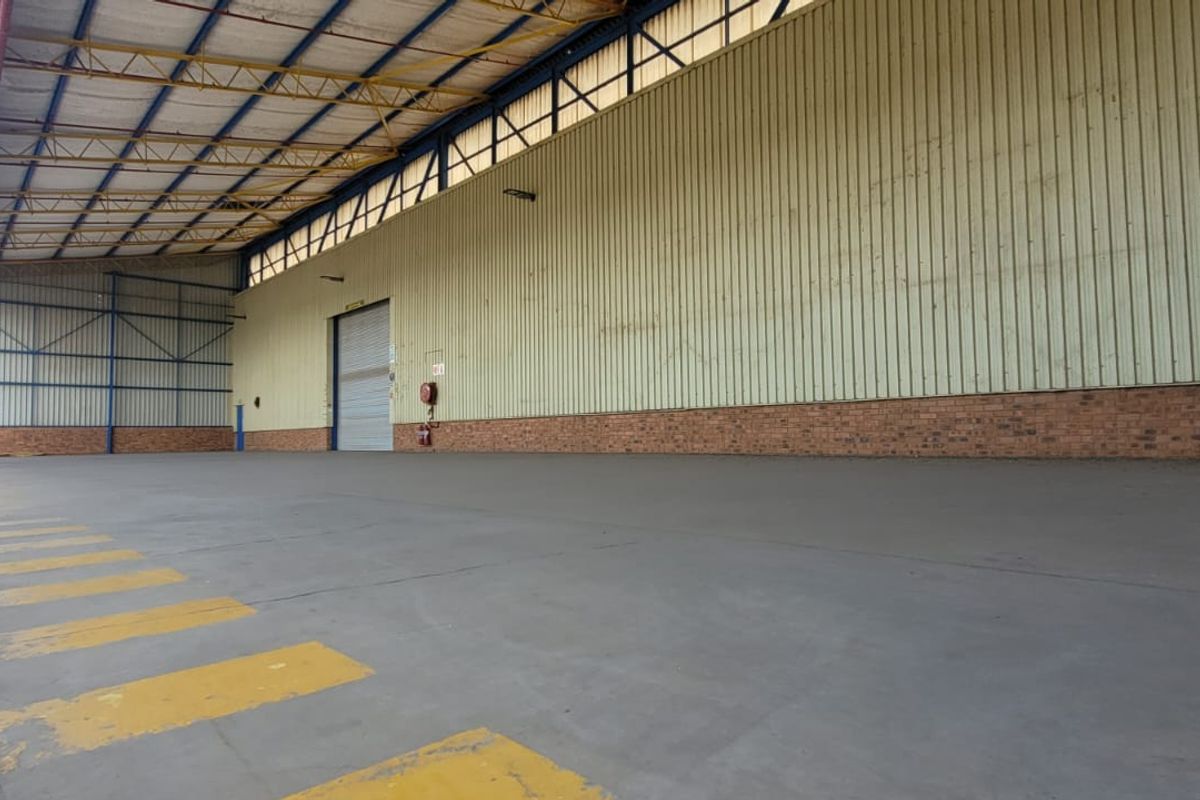 Spacious industrial warehouse unit featuring high ceilings with exposed steel trusses, concrete flooring, and a large roller shutter door for easy access.