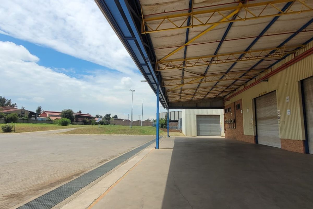 Industrial loading bay area featuring a covered canopy, multiple roller shutter doors, and a spacious concrete hardstand for vehicle access.