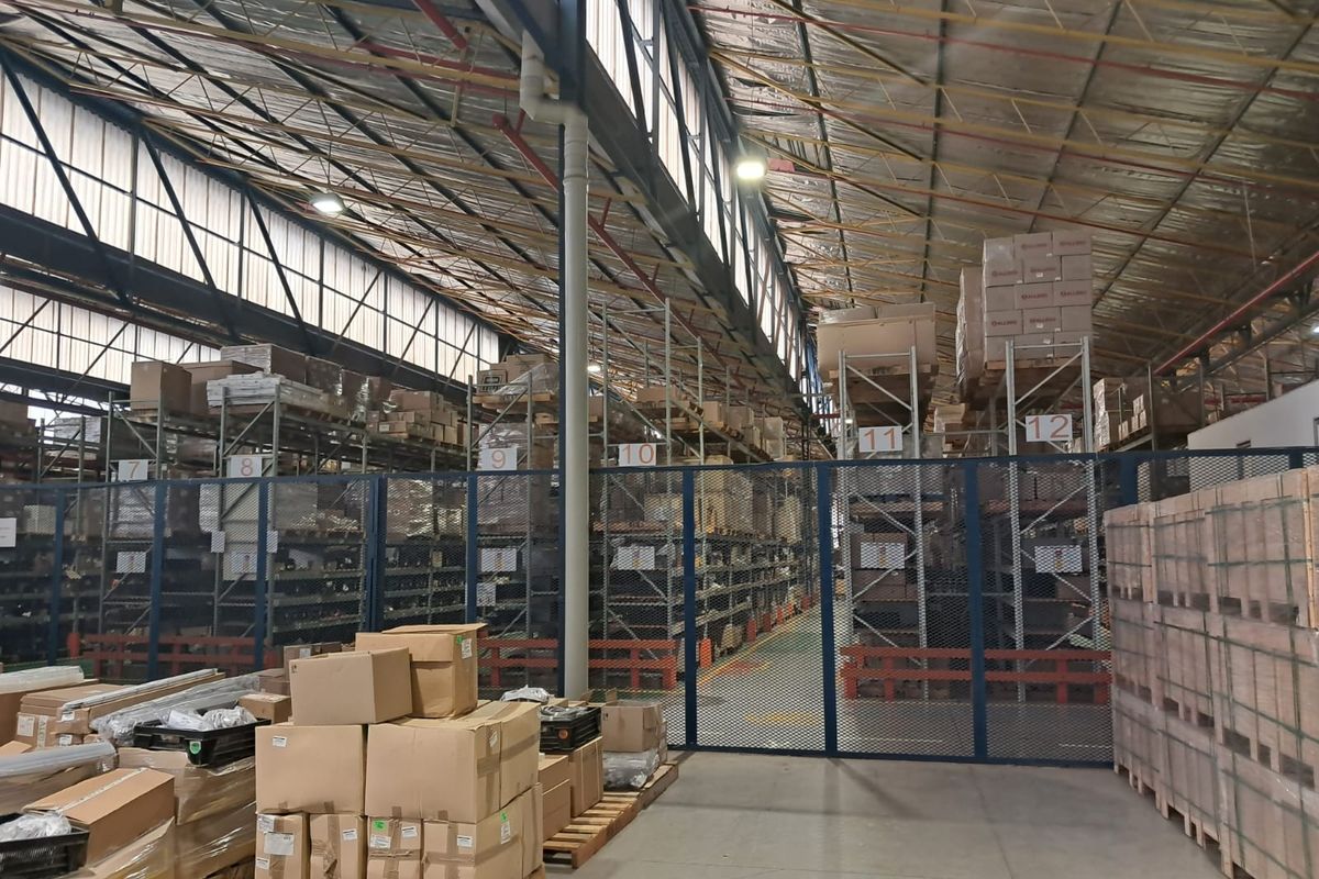 Spacious industrial warehouse featuring high-bay ceilings, concrete flooring, and extensive metal racking systems secured by industrial mesh partitioning.
