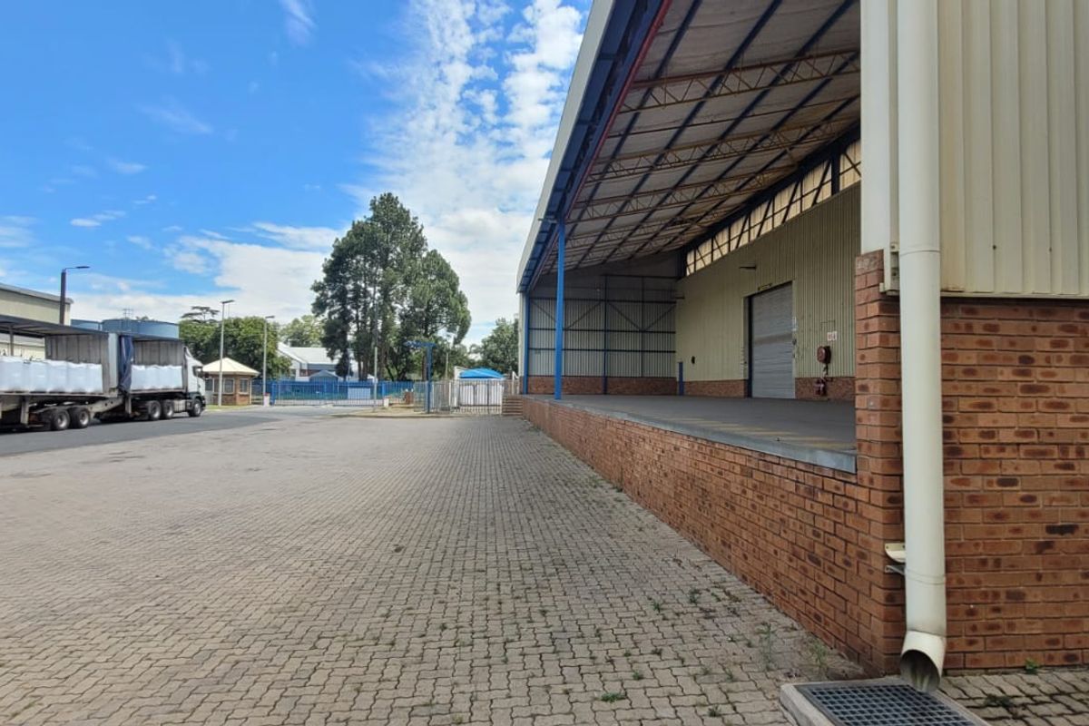 Industrial exterior view featuring a covered loading dock, brick and metal cladding construction, and a spacious paved yard area for logistics.