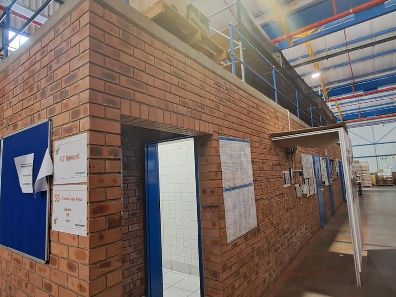 Industrial warehouse interior featuring a brick-built utility structure with a mezzanine level, exposed steel roof trusses, and functional industrial lighting.