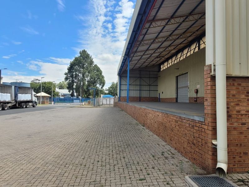 Industrial exterior view featuring a covered loading dock, brick and metal cladding construction, and a spacious paved yard area for logistics.