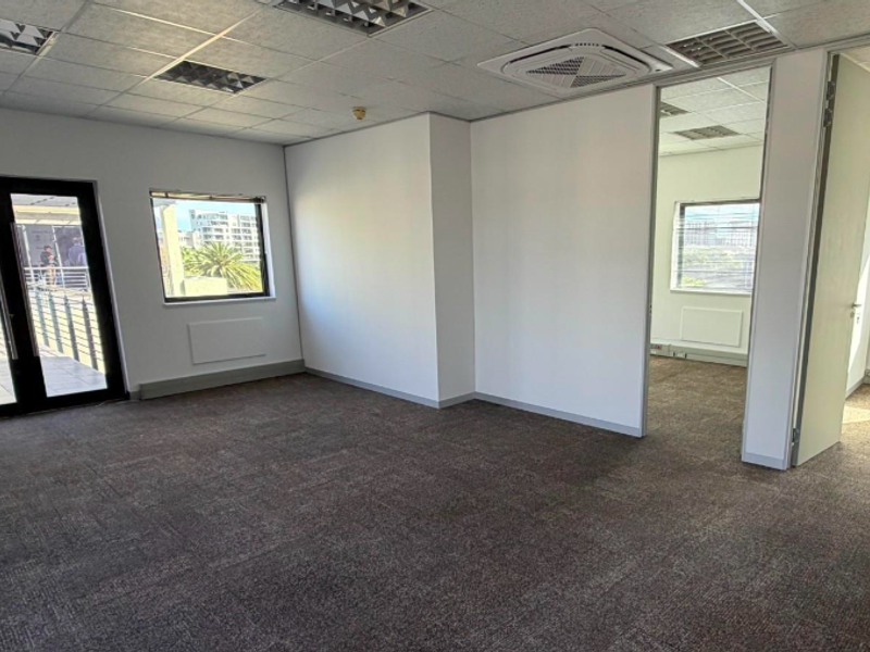 A spacious, empty office suite featuring neutral carpet flooring, suspended ceilings with recessed lighting, and partitioned rooms with access to an outdoor balcony.