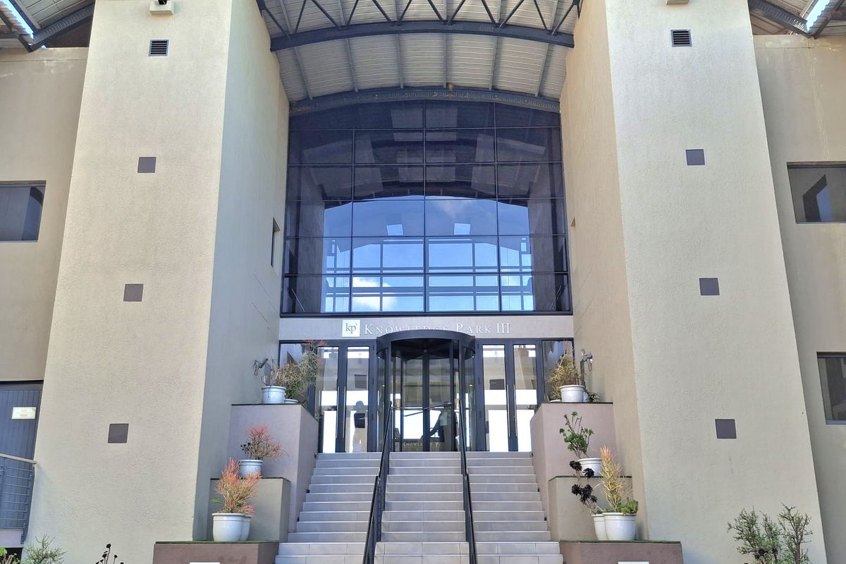 Front elevation of a modern office building featuring a prominent glass entrance, revolving doors, and a grand concrete staircase with metal handrails.