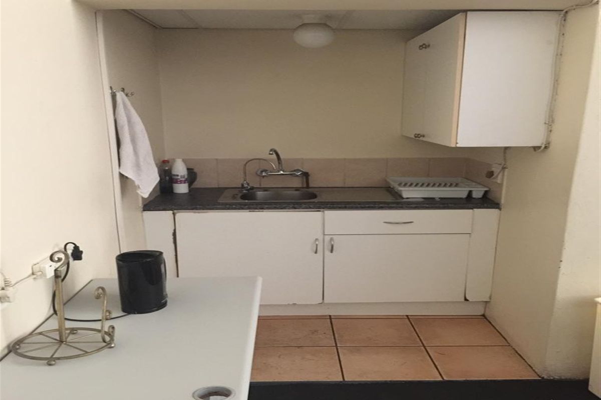 A compact kitchenette featuring white cabinetry, a stainless steel sink, and tiled flooring, suitable for a small office or utility space.