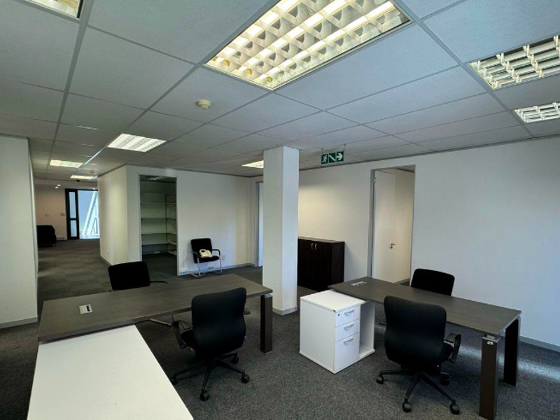 Open-plan office space featuring suspended ceilings with recessed lighting, carpeted flooring, and integrated storage areas, suitable for a professional work environment.