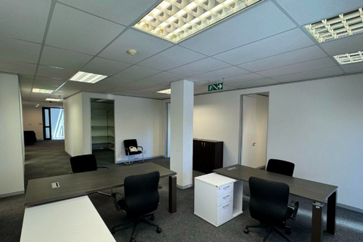 Open-plan office space featuring suspended ceilings with recessed lighting, carpeted flooring, and integrated storage areas, suitable for a professional work environment.