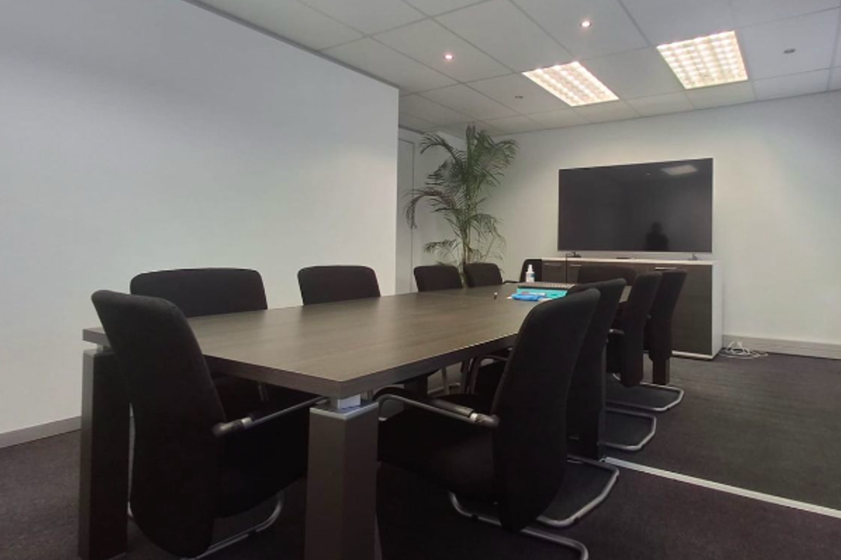 A professional office meeting room featuring a suspended ceiling with recessed lighting, dark carpet flooring, and built-in storage cabinetry.