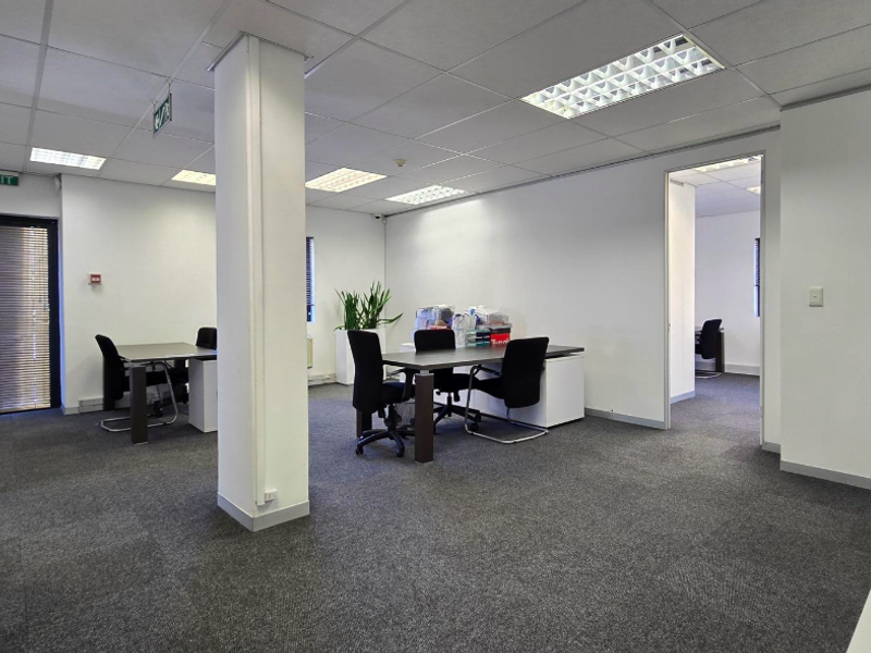 Open-plan office space featuring a suspended ceiling with recessed lighting, carpeted flooring, and a central structural column.