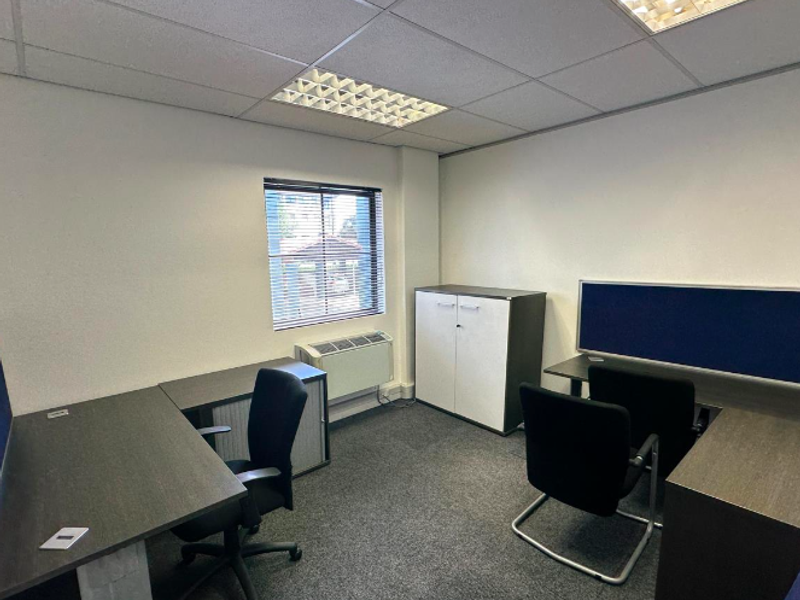 A functional office space featuring a suspended ceiling with recessed lighting, carpeted flooring, and an integrated HVAC unit.