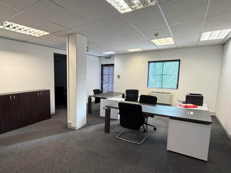 A functional office space featuring a suspended ceiling with recessed lighting, carpeted flooring, and an integrated HVAC unit.