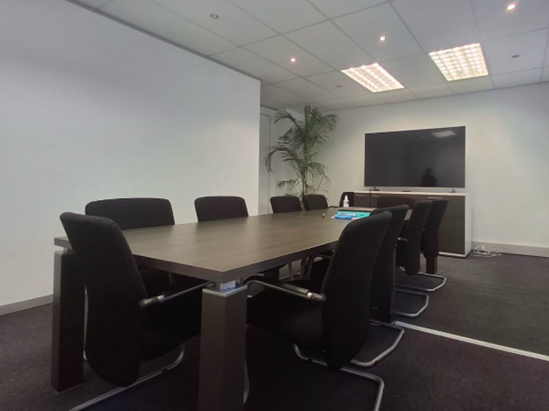 A professional office meeting room featuring a suspended ceiling with recessed lighting, dark carpet flooring, and built-in storage cabinetry.