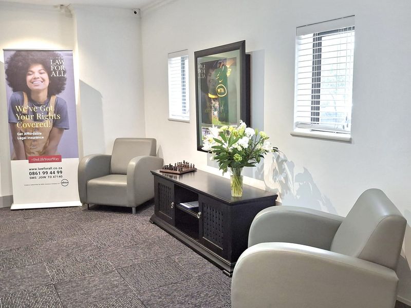 A professional office waiting area featuring carpeted flooring, recessed lighting, and window blinds, providing a clean and functional space for clients.