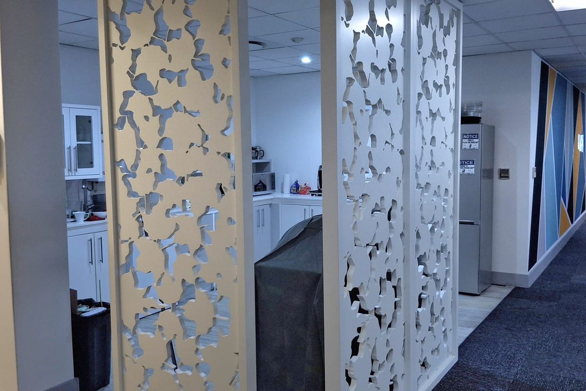 A functional office kitchen area featuring built-in cabinetry and a decorative white privacy screen separating the space from the main hallway.