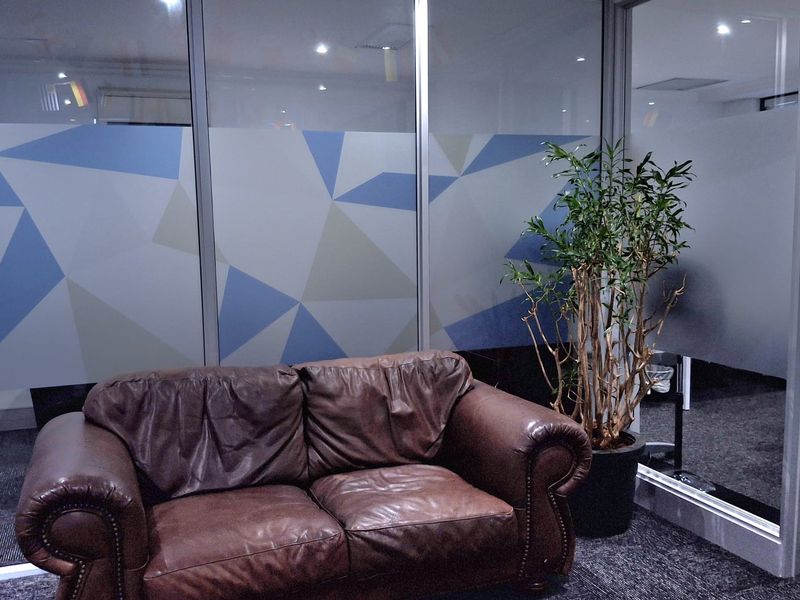 A professional office space featuring modern glass partition walls, recessed ceiling lighting, and durable carpet flooring.