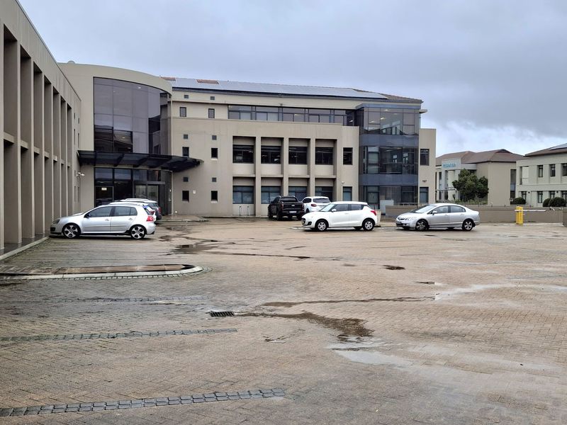 Exterior view of a multi-story office building featuring a paved parking area and modern glass facade elements.