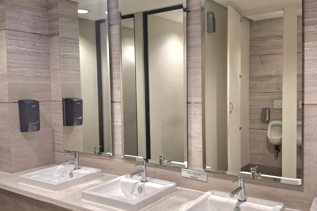 Modern office restroom featuring a triple vanity with stone countertop, integrated sinks, large mirrors, and tiled wall finishes.