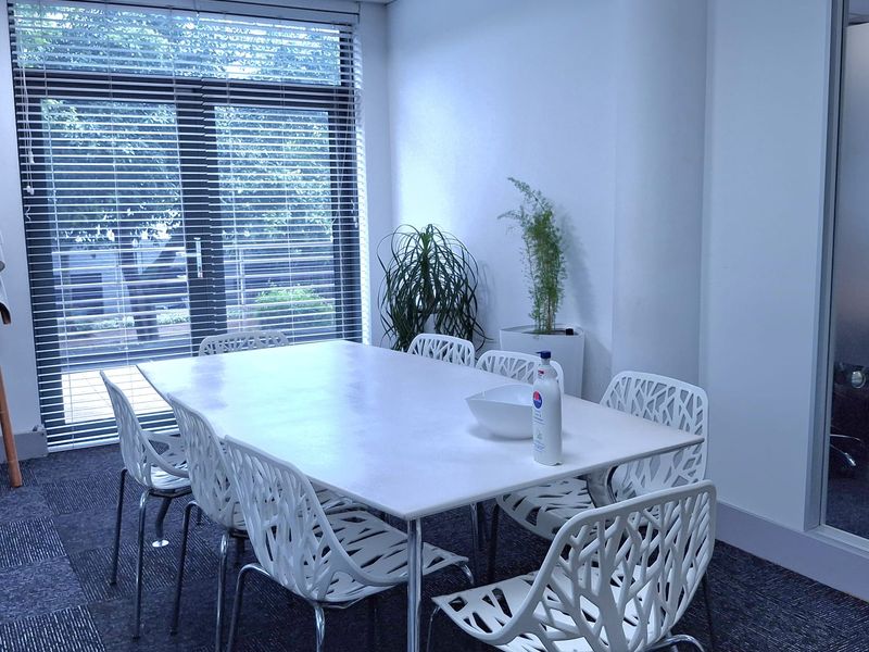 A professional office meeting room featuring carpet tiles, a suspended ceiling with recessed lighting, and a large glass partition wall.