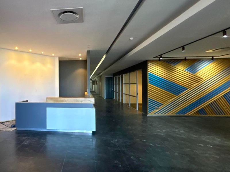 Modern office reception area featuring a built-in desk, decorative wall paneling, glass partitions, and recessed track lighting throughout the open floor space.