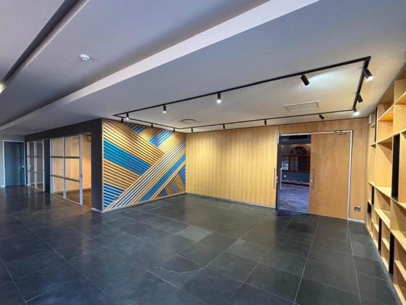 Modern office space featuring high-quality timber wall paneling, built-in shelving, sleek track lighting, and professional glass partitions with dark tiled flooring.