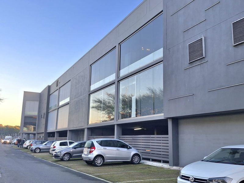 Modern office building exterior featuring a contemporary grey facade, large glass windows, and dedicated ground-level parking bays.