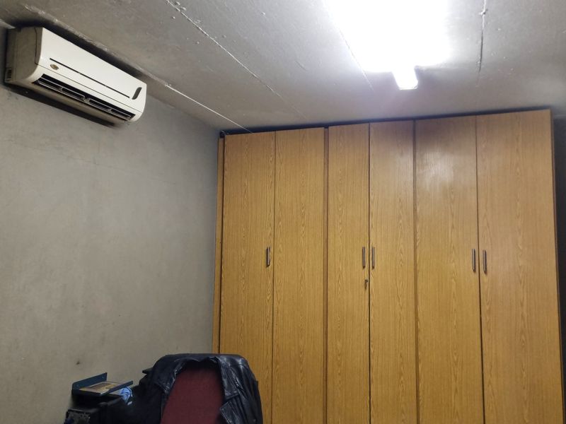 A functional office space featuring extensive built-in wooden cabinetry, an exposed concrete ceiling, and a wall-mounted air conditioning unit.