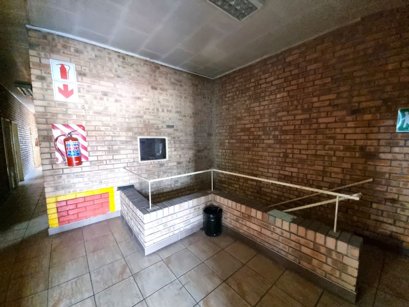 A commercial hallway featuring exposed brick walls, tiled flooring, and a brick balustrade with a metal handrail, equipped with essential fire safety fixtures.