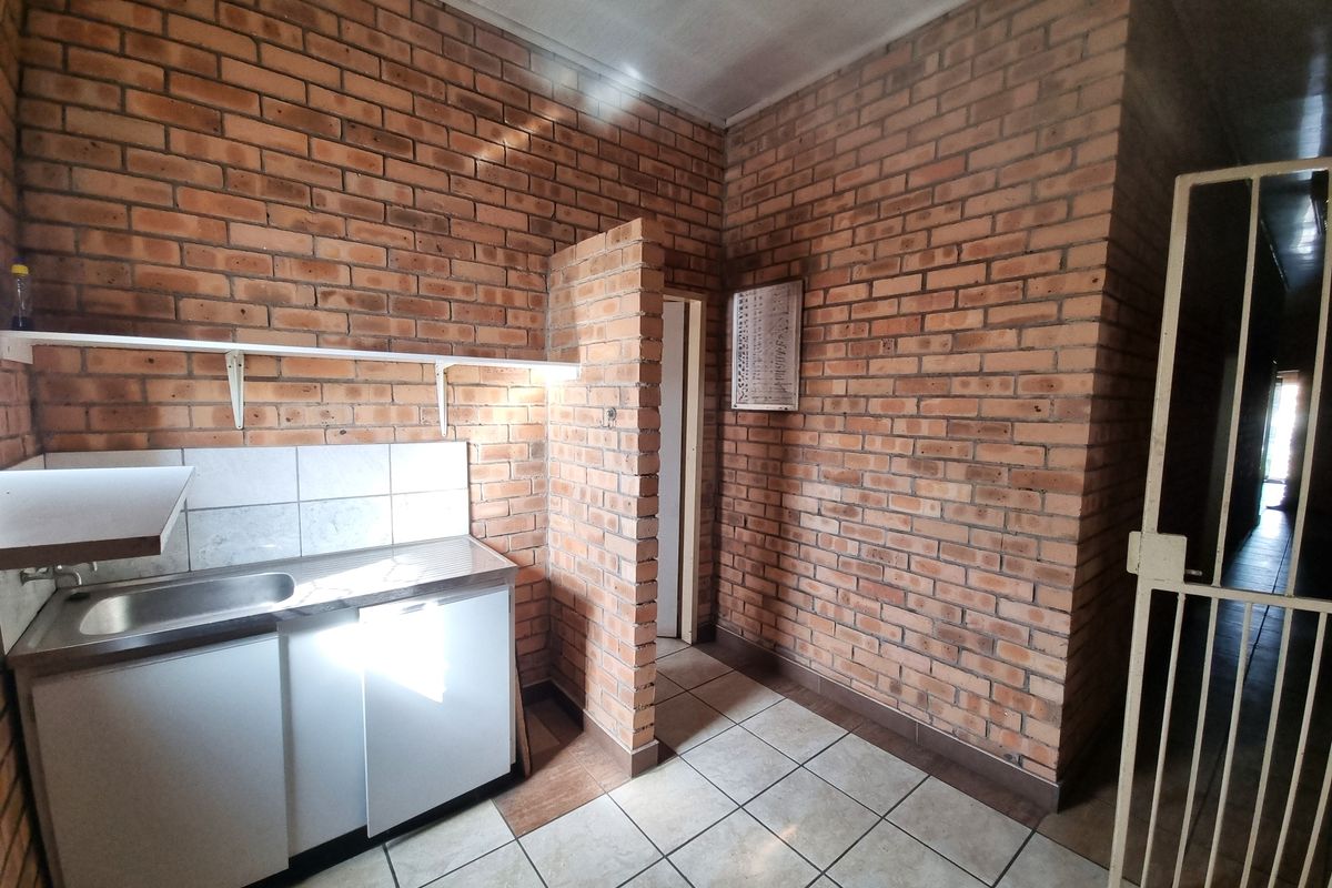 A functional kitchen area featuring exposed brick walls, tiled flooring, a stainless steel sink, and built-in base cabinetry with a tiled splashback.