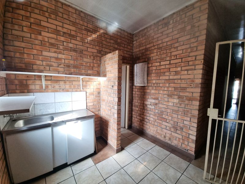 A functional kitchen area featuring exposed brick walls, tiled flooring, a stainless steel sink, and built-in base cabinetry with a tiled splashback.