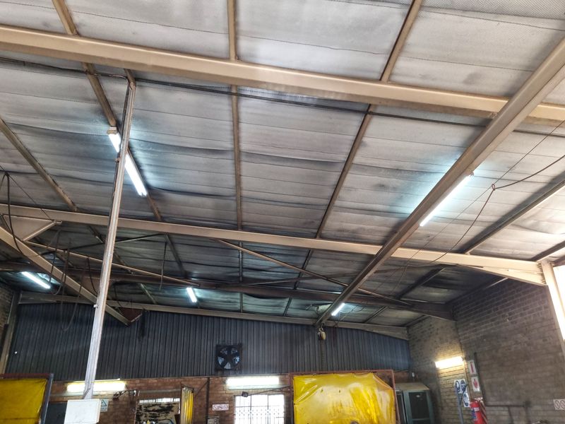 Industrial utility space featuring exposed steel roof trusses, corrugated metal wall cladding, and functional fluorescent lighting.